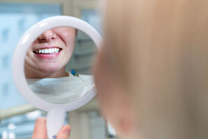 person holding hand mirror, looking at their white teeth