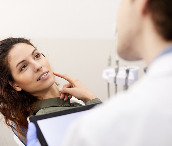 Woman pointing to her cheek while talking to dentist